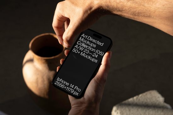 Hand holding smartphone with mockup display, clay pot in background, realistic lighting, suitable for showcasing mobile design mockups for designers.