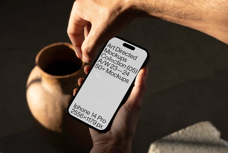 iPhone 14 Pro in person's hand with ceramic vessel blurred in background