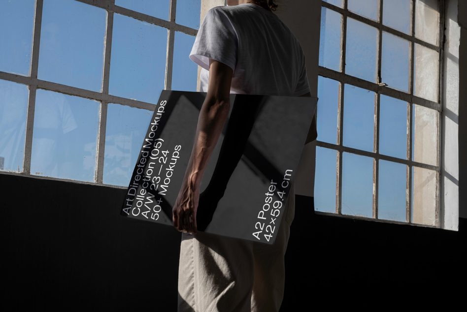 Person holding a large A2 poster mockup in a sunlit room with vintage window, perfect for realistic graphic display presentations.