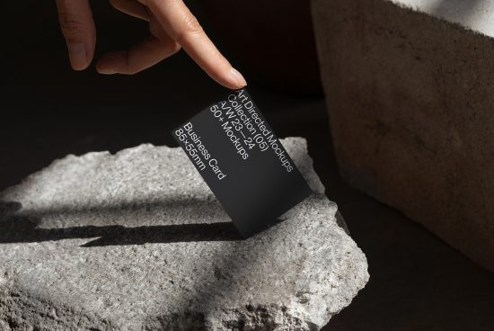 Hand holding a stylish black business card mockup with elegant typography laid on a textured stone, showcasing design and branding.