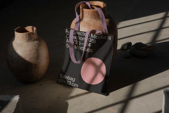 Tote bag mockup in a natural light setting with shadows, next to rustic pottery and smooth stones, demonstrating realistic texture contrast.