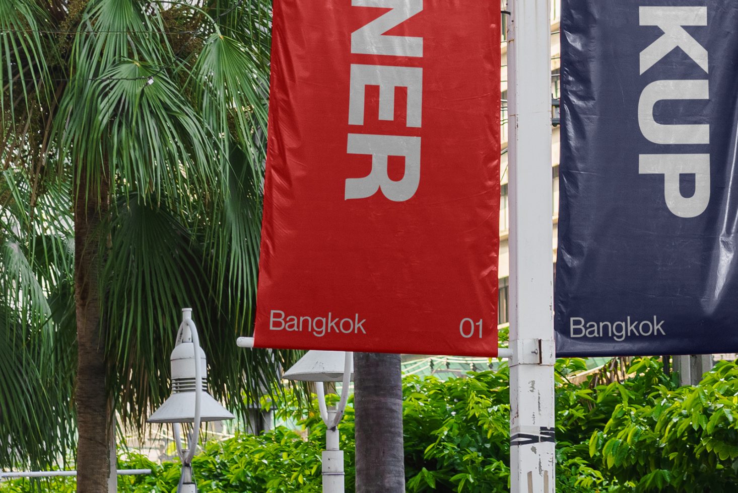 Urban banner mockup with red and blue design elements featuring bold typography, displayed outdoors against a natural background with greenery.