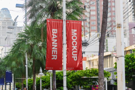 Outdoor vertical banner mockup suspended between palm trees in an urban setting with buildings in background, daylight mockup display.