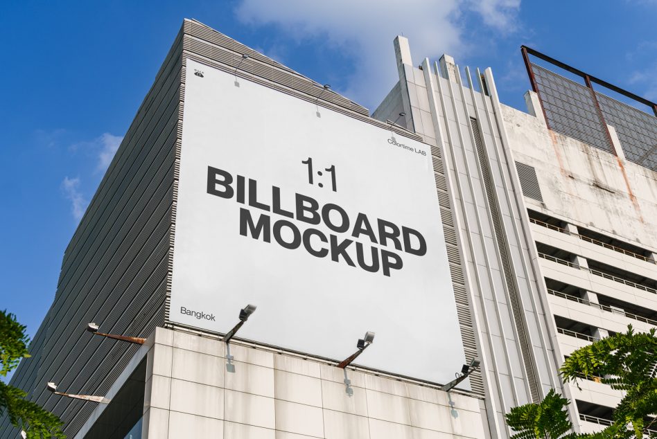 White square billboard mockup on building exterior against blue sky with architectural details visible
