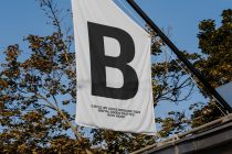 White outdoor flag displaying bold B mark with legal attribution below