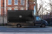 Black delivery truck with blank side panel parked on city street near brick building