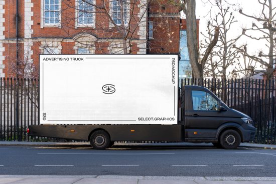Mockup of black advertising truck with blank side for graphic design display parked on street with buildings and trees in background.