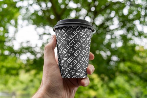 Hand holding a paper cup with custom typography design mockup, bokeh green background, ideal for branding presentations and graphics.