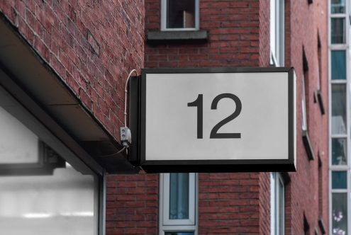 Outdoor hanging signage mockup with brick wall background, displaying the number 12, for urban design presentations.