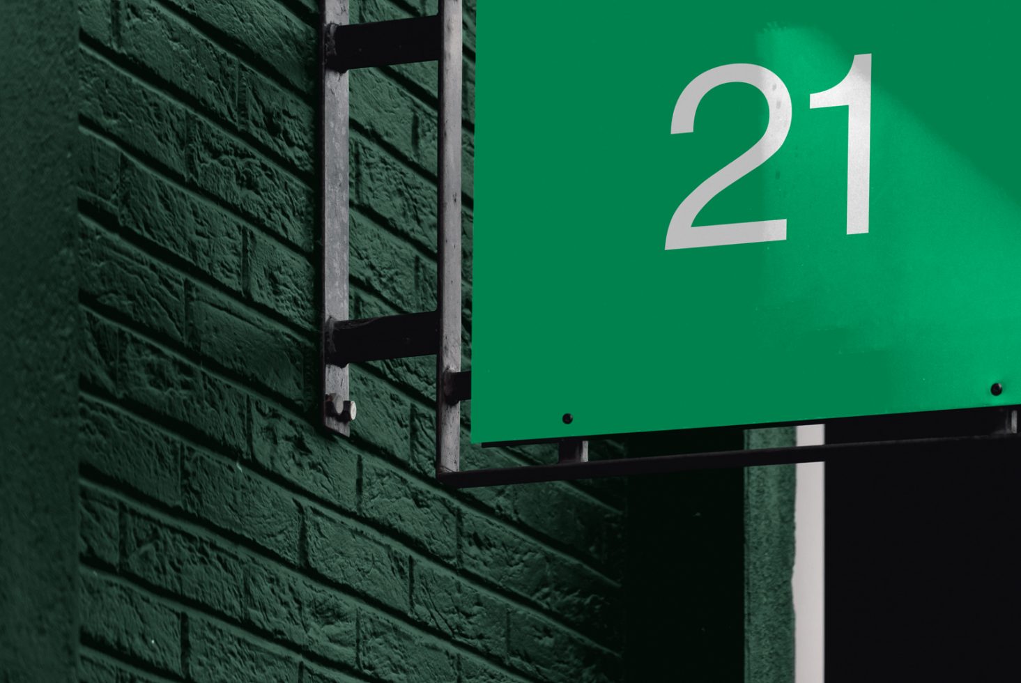 Green number 21 sign on a textured brick wall for graphic design mockup with strong contrast and urban feel.