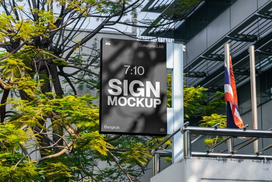 Outdoor hanging sign mockup displayed on a metal frame in an urban setting with greenery and glass facade, ideal for designers.