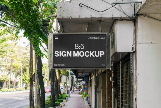 Urban street sign mockup hanging on a building facade with greenery and sidewalk in the background, ideal for branding presentation.
