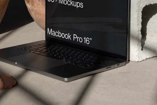 Macbook Pro mockup on concrete surface near pot, angled view, showcasing screen and keyboard for digital asset designers.