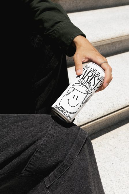 Hand holding custom-designed coffee can mockup with cheerful graphics, highlighting product branding and packaging design for creative assets.