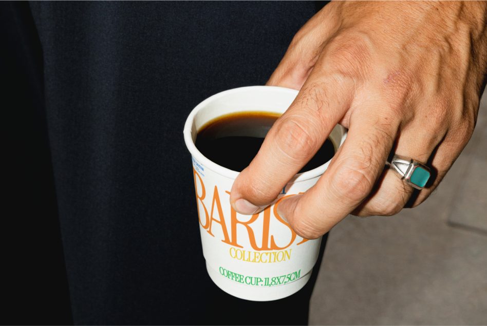Close shot of hand holding cup showing orange Barista Collection lettering on dark fabric