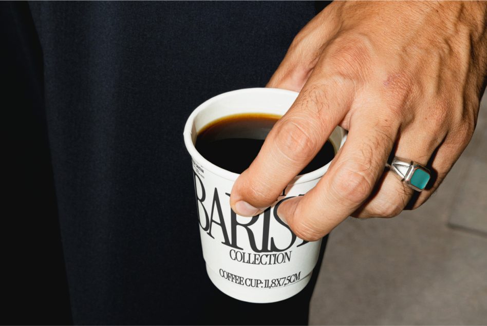Person gripping white coffee cup with black Barista Collection text against dark background