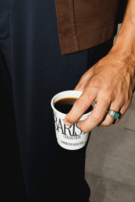 Man in dark cardigan holding coffee cup with Barista Collection logo while standing
