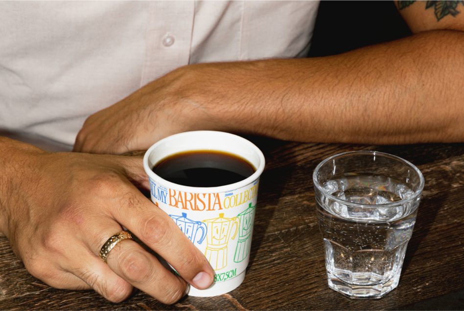 Close-up photorealistic mockup of a person's hand holding a coffee mug next to a water glass on a wooden table suitable for branding presentations.