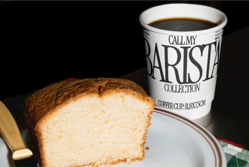 Paper coffee cup with bold font on table next to cake slice, ideal for mockup graphics and print design for cafes and bars.