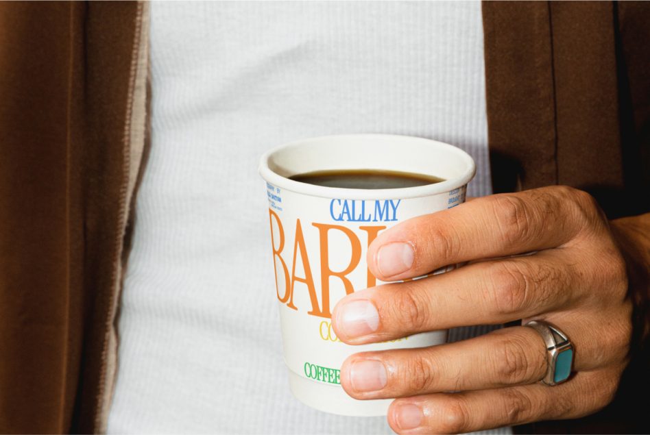 Close-up view of a person holding a paper coffee cup with a custom typographic design, ideal for mockup, print design, and branding visuals.