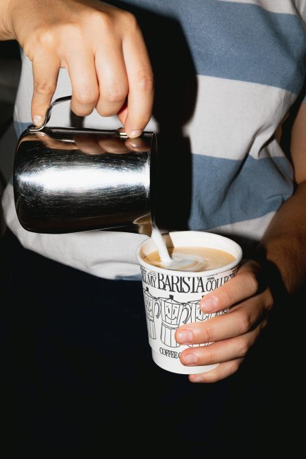 Person pouring milk into coffee cup creating latte art, ideal for Mockups and Advertising Templates with a cafe and barista theme.