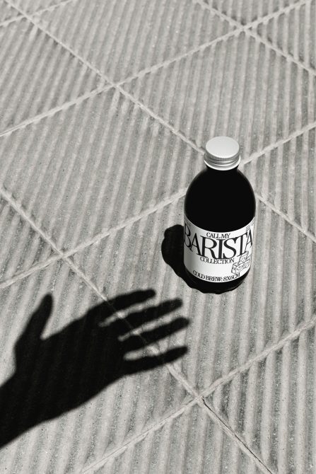 Overhead shot of cold brew bottle on textured concrete with hand shadow
