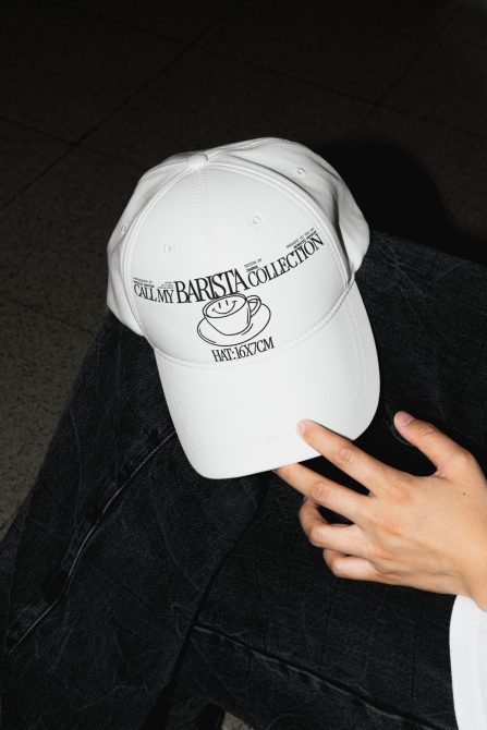 White baseball cap with Call My Barista Collection branding held by hand