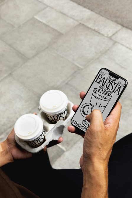 Two white coffee cups with Barista branding held next to iPhone app mockup on tile