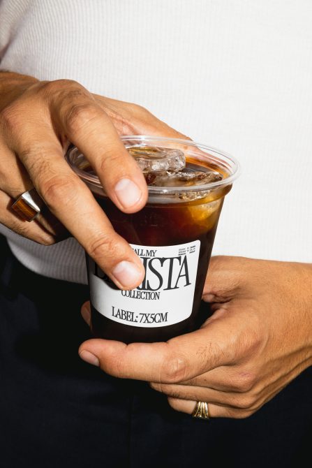 Close-up of hands holding iced coffee mockup with editable label for packaging design presentation.