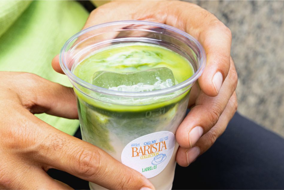 Hands holding clear cup with matcha latte labeled Call My Barista Collection in orange