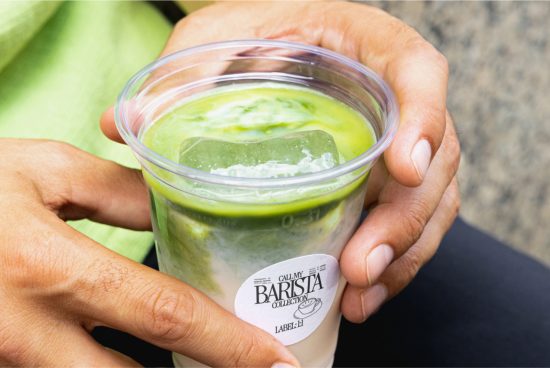 Close-up of hands holding a matcha latte cup with a label mockup on a blurred green background. Ideal for beverage branding presentation.