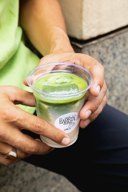 Hands holding clear cup with matcha latte labeled Call My Barista Collection