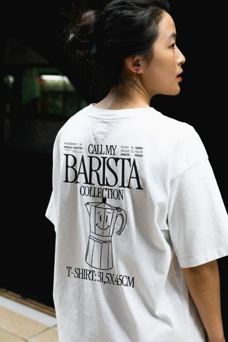 Woman in white t-shirt with barista design, mockup for graphic print, trendy apparel presentation, dimensions label visible.