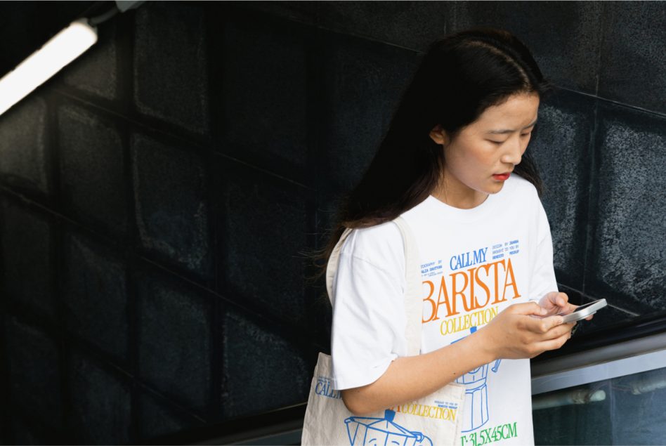 Woman in white graphic t-shirt using smartphone, urban background, potential for mockups and apparel design templates for designers.