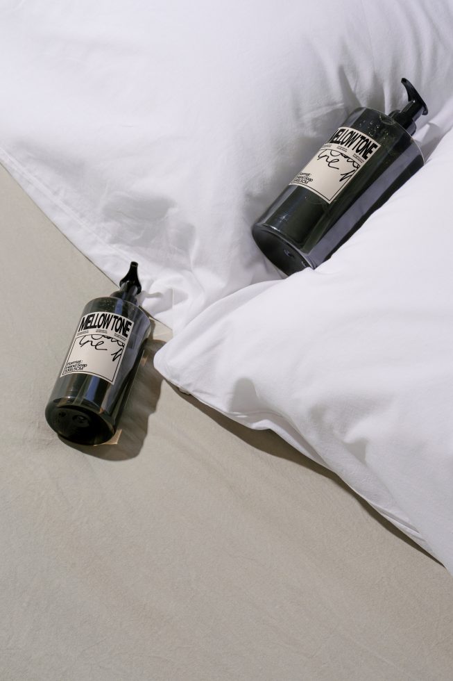 Elegant product mockup featuring two cosmetic bottles on a white bed sheet, perfect for showcasing label designs for designers.