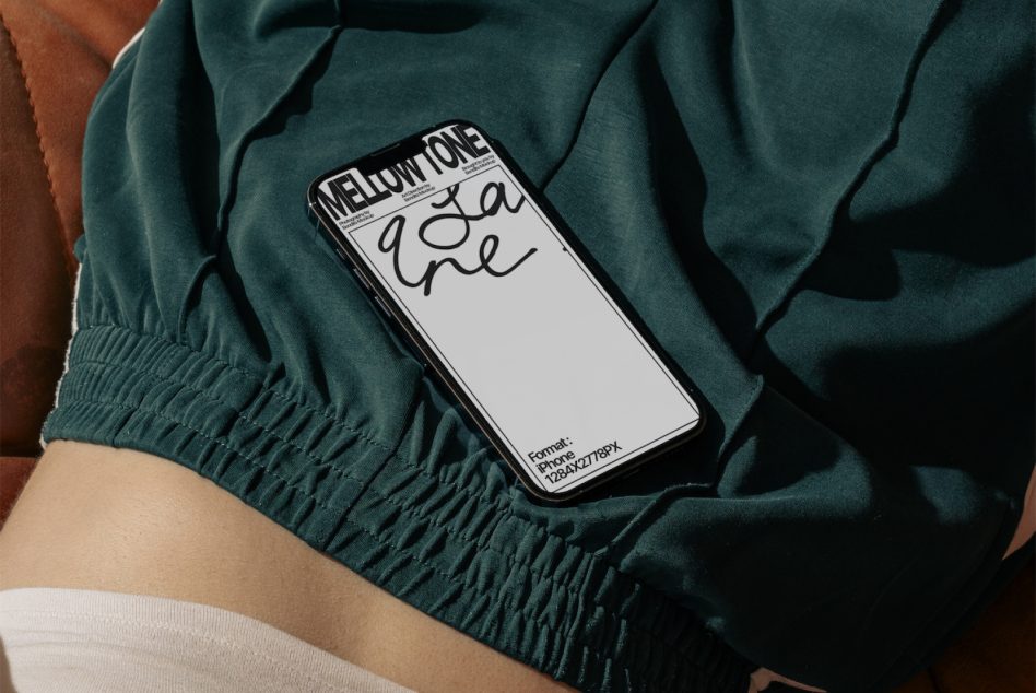 Hand holding phone mockup with white screen resting on teal fabric