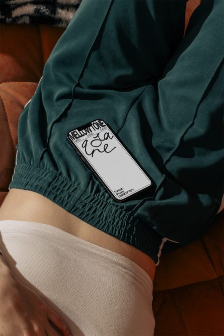 Hand holding phone mockup with white screen resting on teal fabric