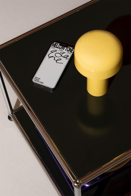 Minimalist smartphone mockup on a glossy black surface with a yellow lamp, showcasing screen design, ideal for graphic designers and ad presentations.