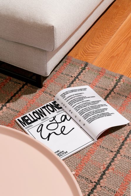 Magazine mockup on textured rug beside sofa, displaying bold typography and modern layout, perfect for design presentations and portfolios.