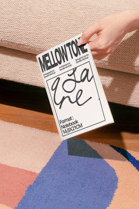 Hand holding white notebook mockup over colorful geometric fabric background
