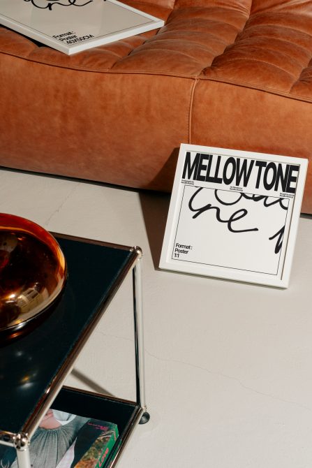Mellow Tone poster on white table by cognac bowl near tan leather couch