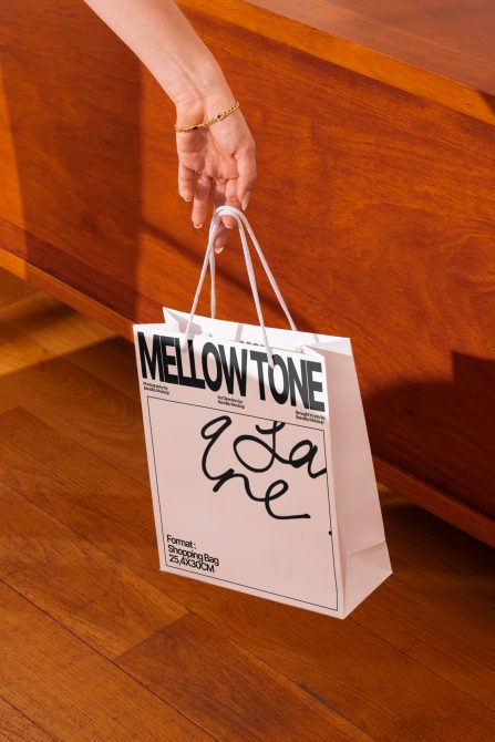 Shopping bag mockup held by a hand. Shows customizable design, elegant font, realistic wooden background for product presentation.