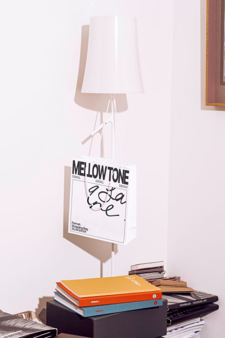 Minimalist shopping bag mockup hanging from white lamp with books stacked below
