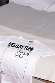 White t-shirt flat lay with Mellow Tone branding on gray bed sheet backdrop