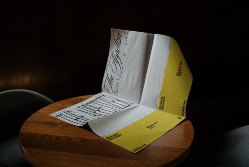 Curved brochure mockup on a wooden table showcasing elegant typography design for font presentation, visualized in a moody lighting setting.