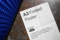 White A3 folded poster with metal texture floor in background