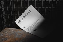 Tilted white A4 letterhead on rusty metal surface with grid backdrop