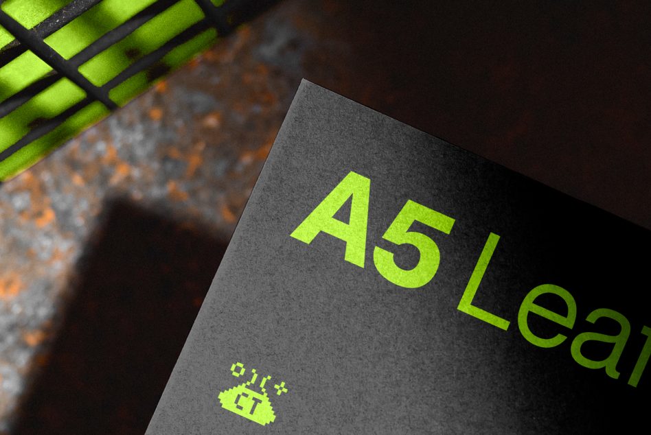 Mockup of an A5 flyer with neon text design, showcasing font style and print quality on textured paper with a blurred industrial background.