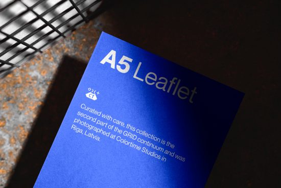 Blue A5 leaflet mockup with text, positioned on a textured surface next to a wireframe object, showcasing professional presentation for design assets.