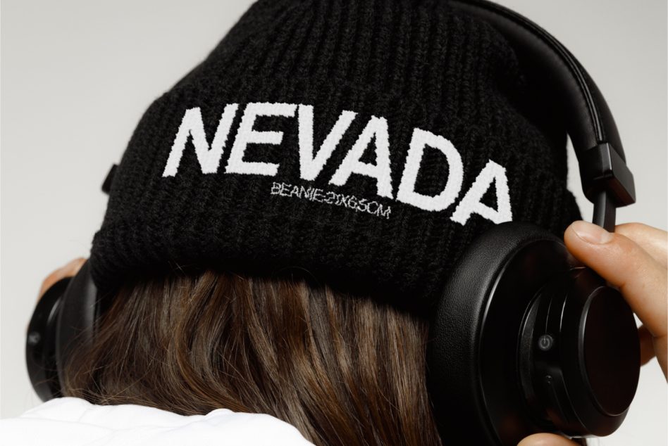 Person wearing a knitted beanie with NEVADA text design and headphones, mockup for beanie branding presentations.